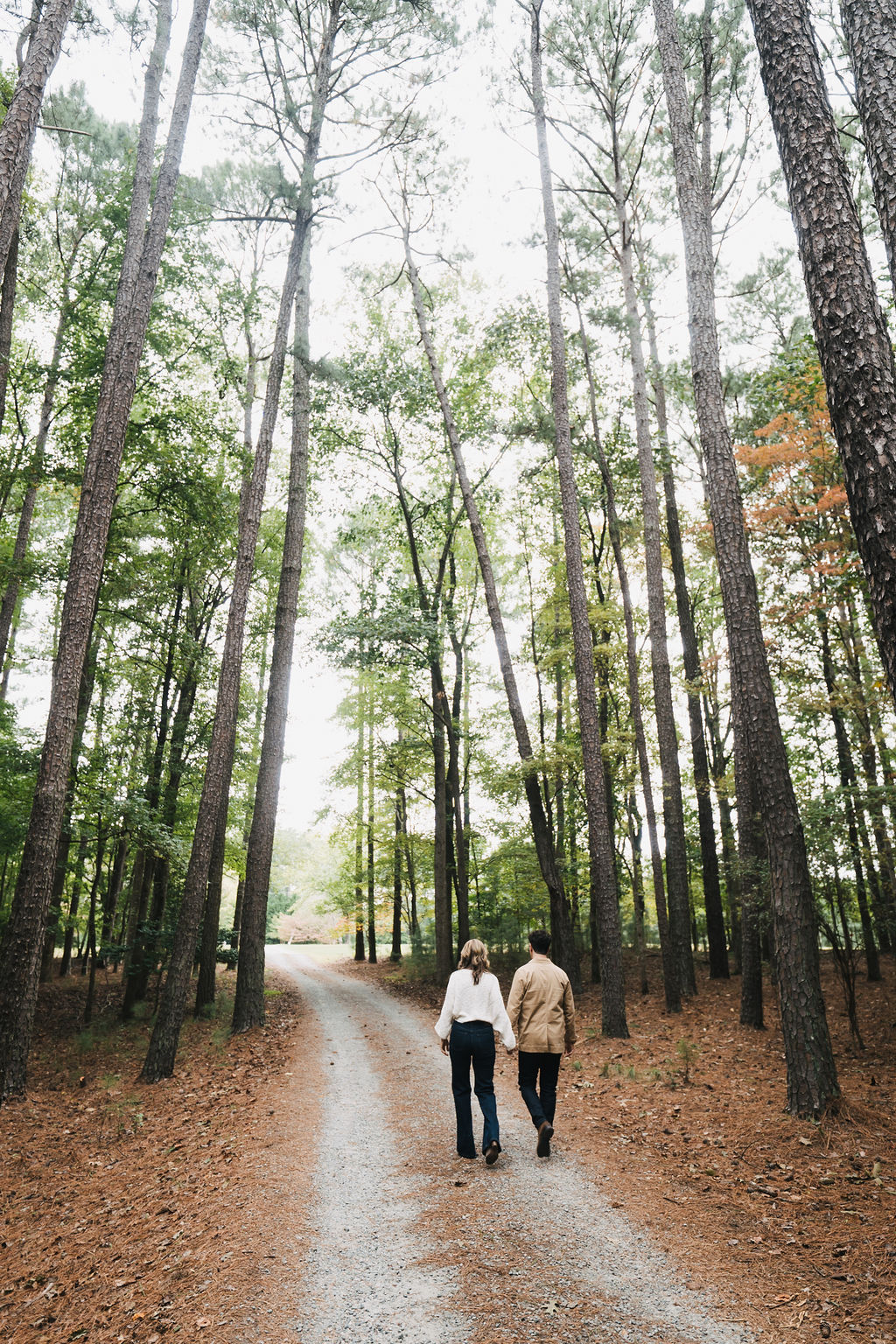 Steve and Lisa walking on a gravel road with tall trees all around them.