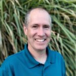 Life Coach wearing a blue shirt and smiling. Standing in front of palm trees.